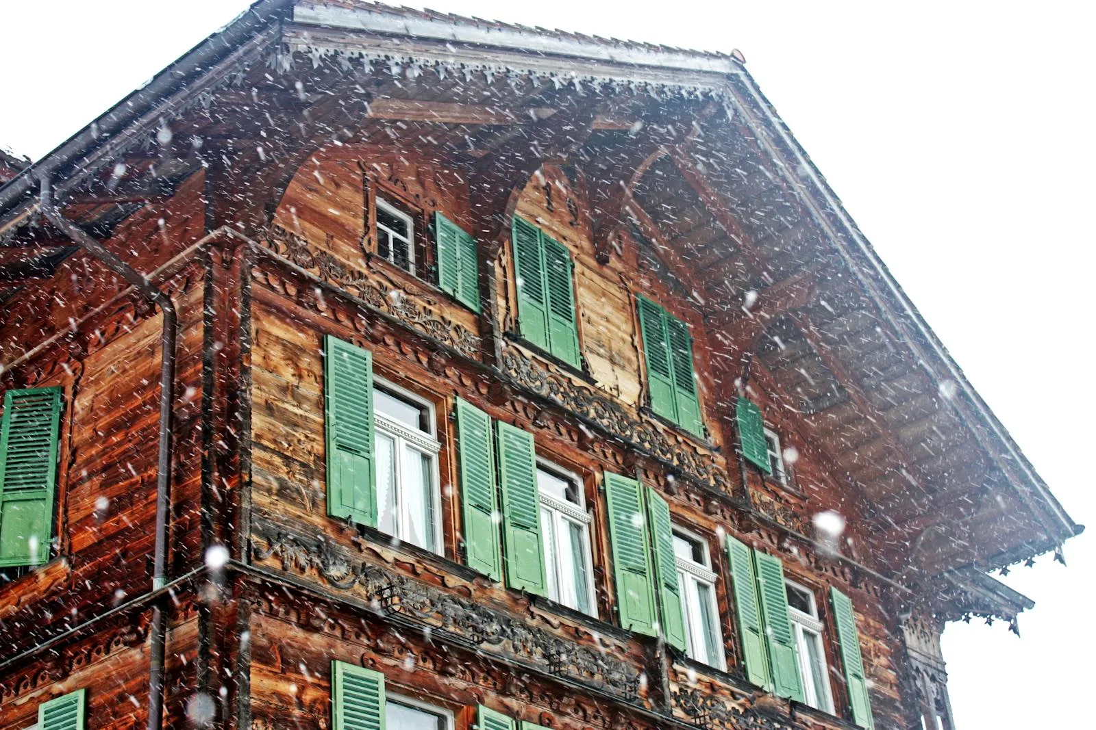 Traditional Bernese chalet with wooden facade and green shutters in snowfall