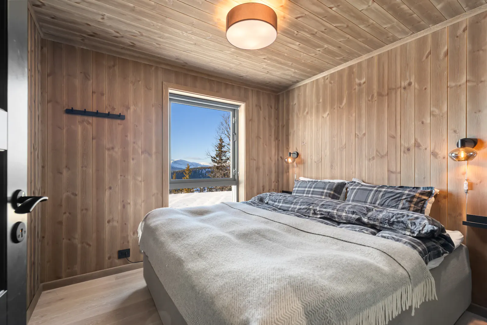 Schlafzimmer mit Arvenholz-Wand- und Deckenverkleidung und Bergblick durchs Fenster